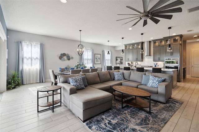 living room with a textured ceiling, ceiling fan with notable chandelier, light hardwood / wood-style floors, and plenty of natural light