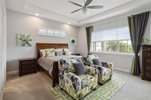 bedroom featuring ceiling fan, multiple windows, a raised ceiling, and light colored carpet