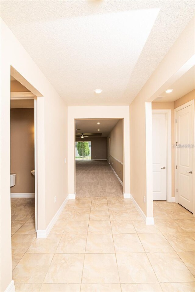 hall with a textured ceiling and light tile patterned floors