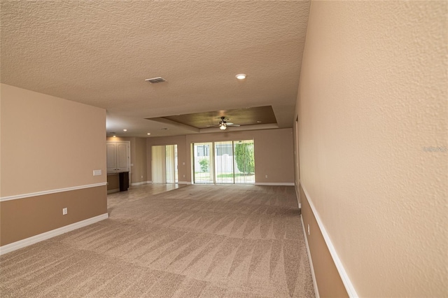 spare room with a textured ceiling, carpet, ceiling fan, and a raised ceiling