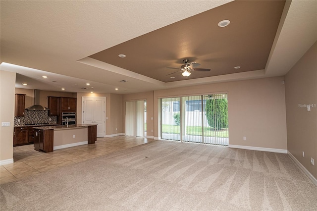 unfurnished living room featuring a textured ceiling, light carpet, ceiling fan, and a raised ceiling