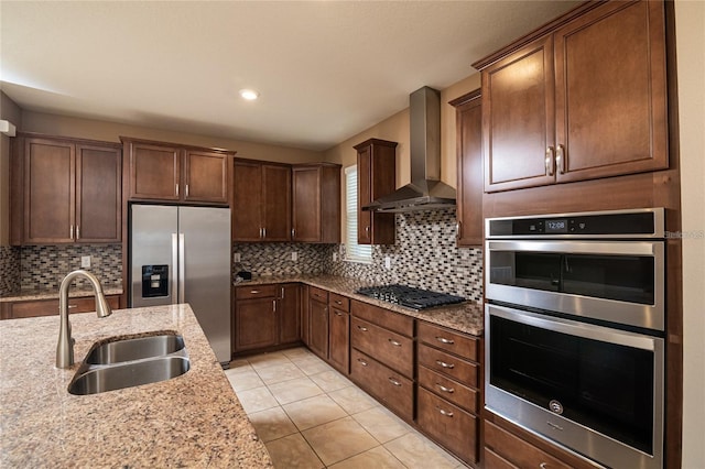 kitchen featuring light stone counters, stainless steel appliances, decorative backsplash, sink, and wall chimney exhaust hood