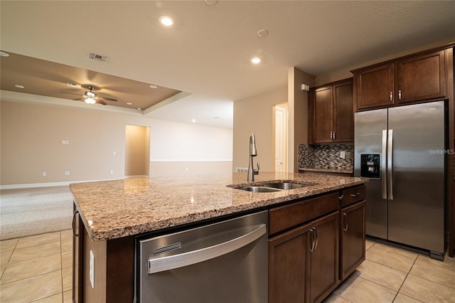 kitchen featuring stainless steel appliances, light stone countertops, sink, ceiling fan, and a kitchen island with sink