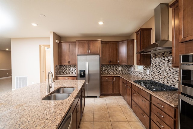 kitchen featuring light stone counters, sink, tasteful backsplash, wall chimney range hood, and appliances with stainless steel finishes