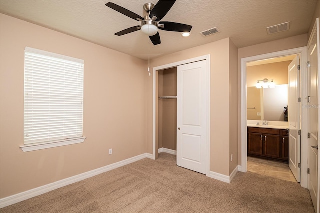 unfurnished bedroom with a closet, connected bathroom, a textured ceiling, light carpet, and ceiling fan