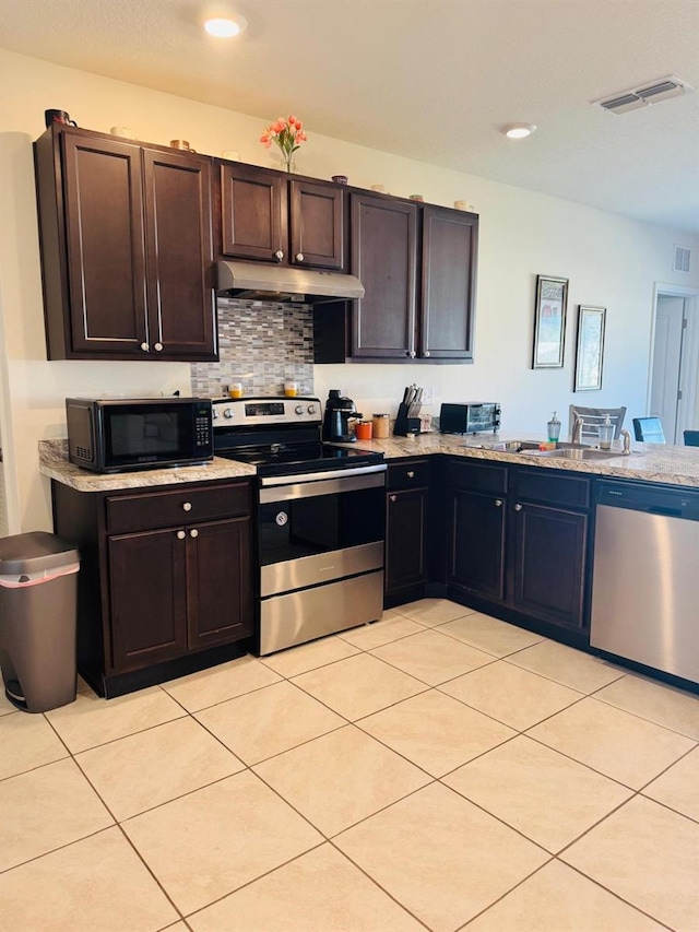 kitchen with light stone countertops, light tile patterned flooring, dark brown cabinets, and appliances with stainless steel finishes