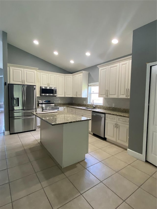 kitchen featuring a kitchen island, white cabinetry, appliances with stainless steel finishes, light stone countertops, and lofted ceiling