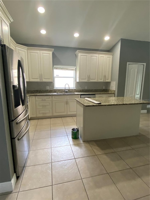 kitchen with sink, appliances with stainless steel finishes, dark stone counters, light tile patterned floors, and a center island