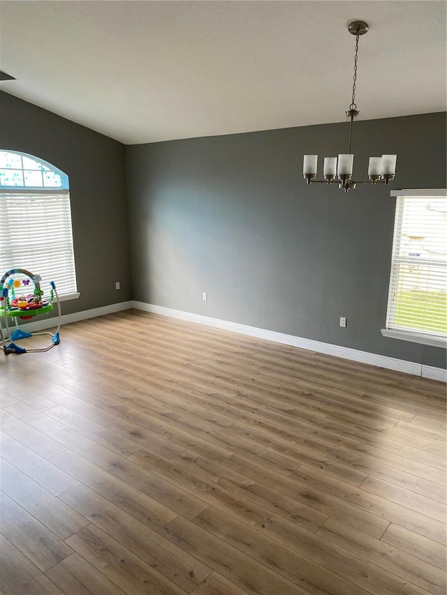 unfurnished room with an inviting chandelier, a wealth of natural light, and hardwood / wood-style floors