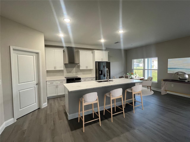 kitchen featuring white cabinets, black appliances, wall chimney range hood, and an island with sink