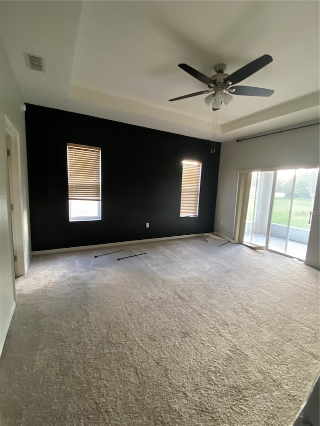 empty room featuring ceiling fan, a tray ceiling, light carpet, and a healthy amount of sunlight