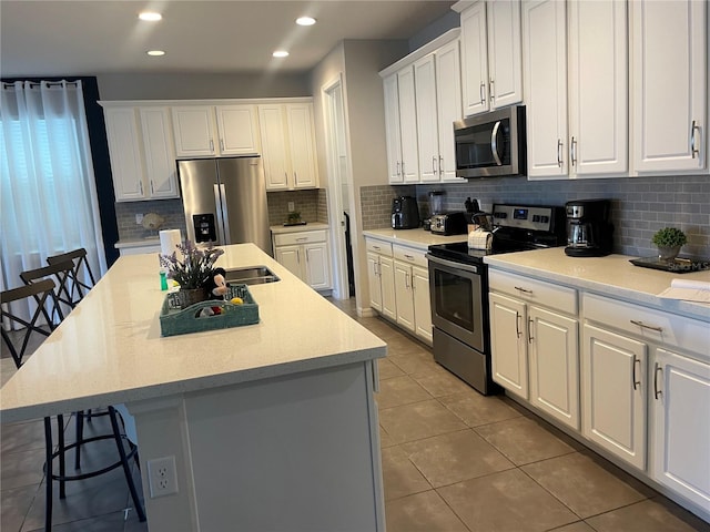 kitchen with a kitchen island with sink, a kitchen breakfast bar, stainless steel appliances, and white cabinets