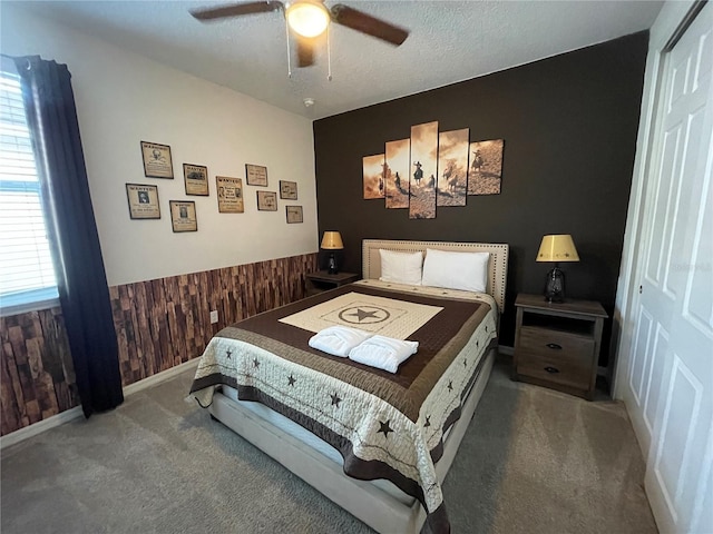 carpeted bedroom featuring a closet, wooden walls, a textured ceiling, and ceiling fan