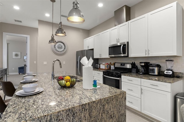 kitchen with decorative light fixtures, stainless steel appliances, a kitchen island with sink, and dark stone countertops