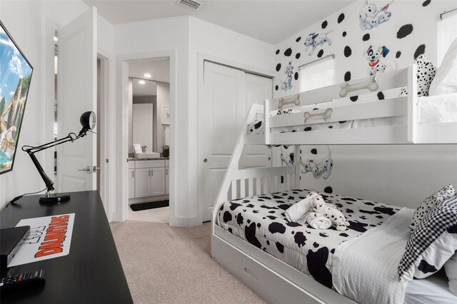 bedroom with light colored carpet, ensuite bath, a closet, and sink