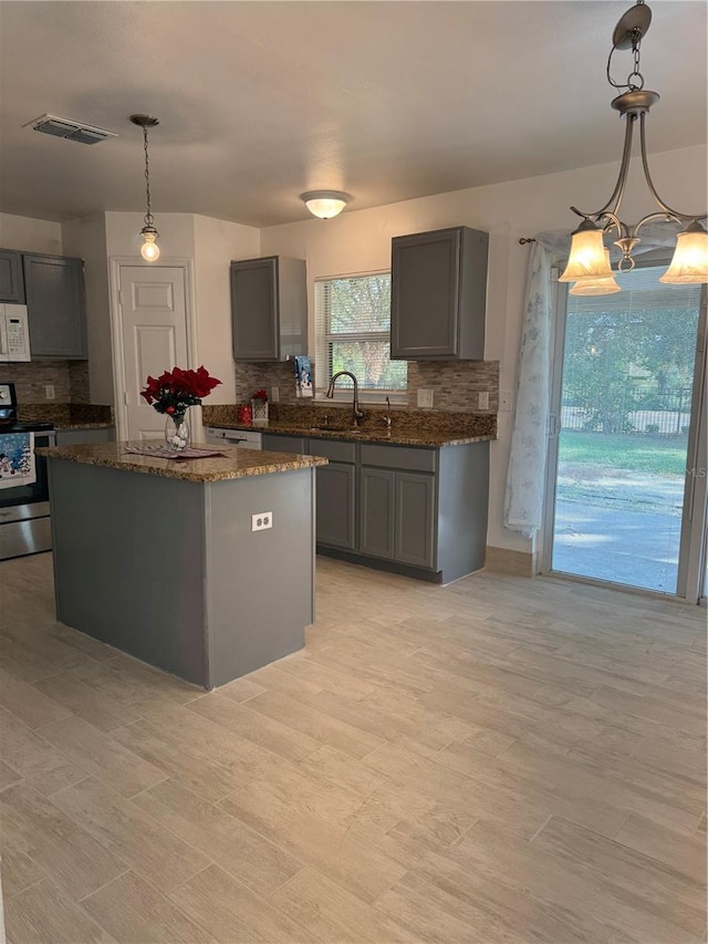 kitchen with decorative backsplash, decorative light fixtures, a center island, gray cabinets, and stainless steel range with electric cooktop