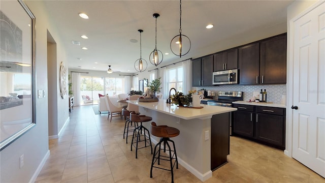 kitchen with stainless steel appliances, a kitchen breakfast bar, ceiling fan, decorative light fixtures, and an island with sink