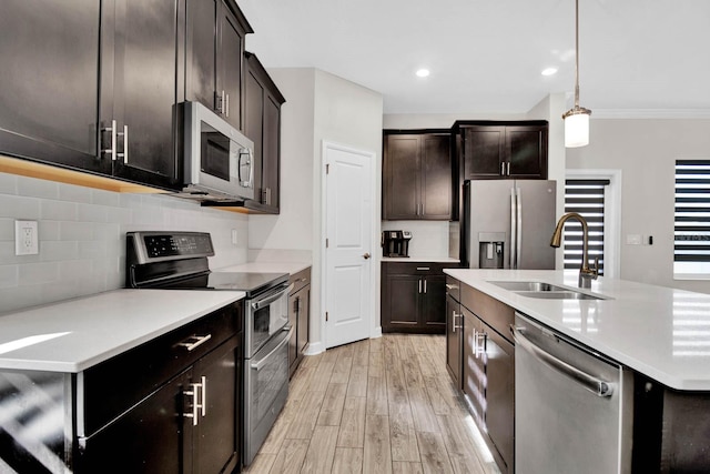 kitchen featuring appliances with stainless steel finishes, light wood-type flooring, ornamental molding, sink, and decorative light fixtures