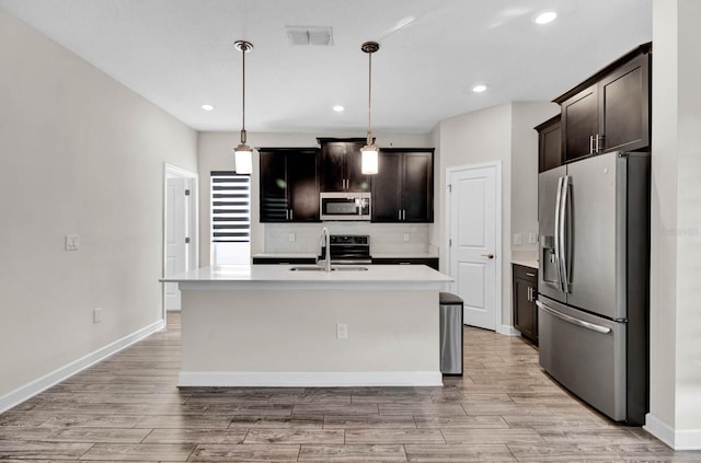 kitchen featuring sink, hanging light fixtures, stainless steel appliances, light hardwood / wood-style flooring, and a kitchen island with sink