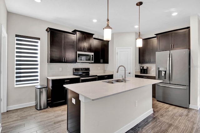 kitchen featuring sink, pendant lighting, light hardwood / wood-style floors, a kitchen island with sink, and appliances with stainless steel finishes