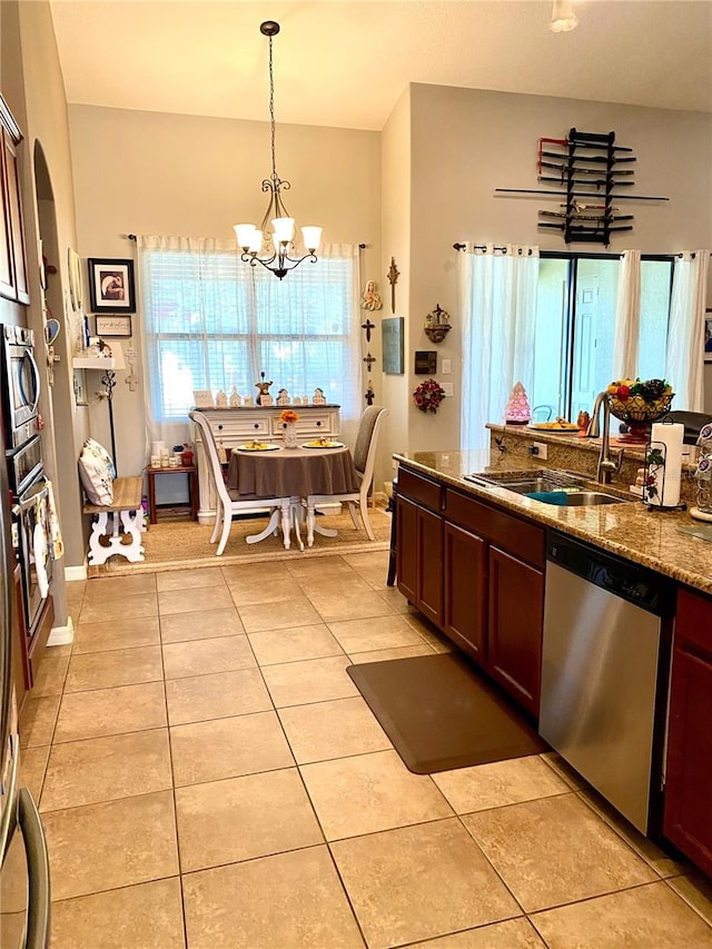 kitchen featuring an inviting chandelier, hanging light fixtures, stainless steel dishwasher, dark stone countertops, and light tile patterned floors