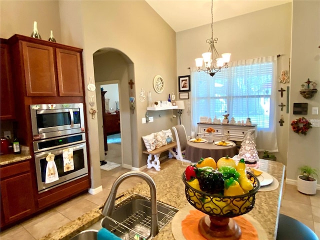 kitchen with light tile patterned floors, stainless steel appliances, an inviting chandelier, and light stone counters