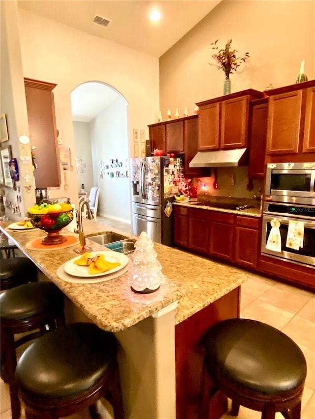 kitchen with light stone countertops, appliances with stainless steel finishes, a kitchen breakfast bar, sink, and light tile patterned flooring