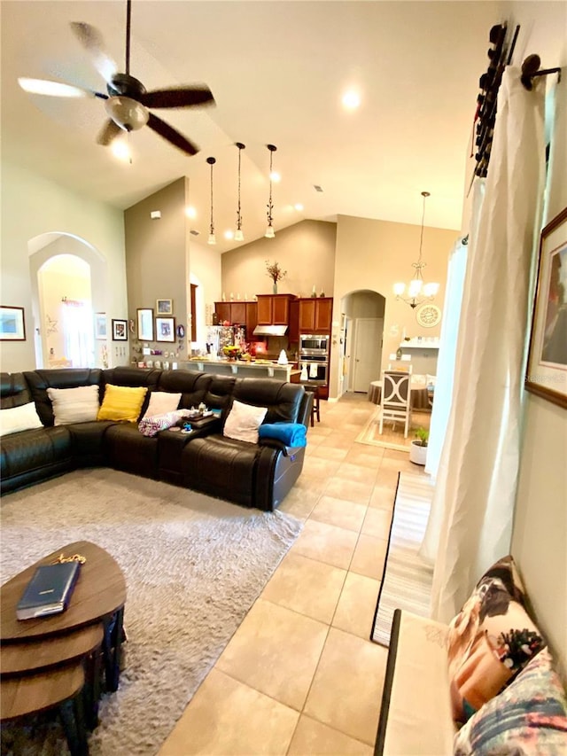 tiled living room with ceiling fan with notable chandelier and high vaulted ceiling