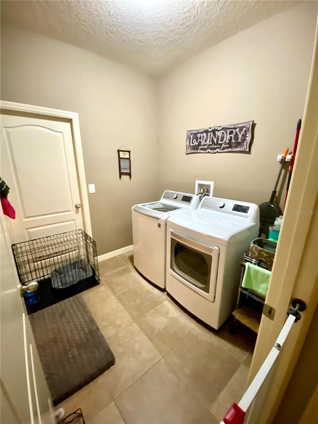 laundry area featuring washing machine and clothes dryer, light tile patterned flooring, and a textured ceiling