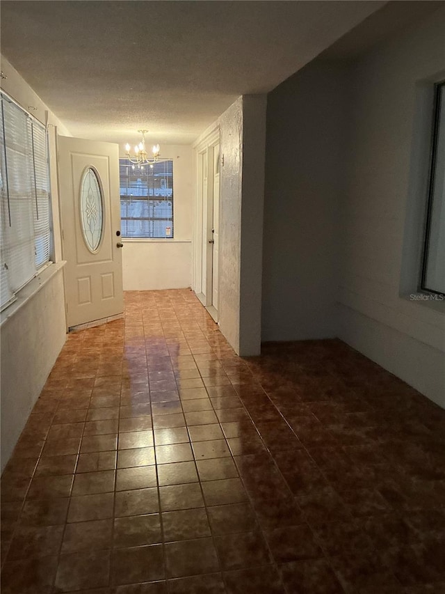 hallway featuring a textured ceiling, dark tile patterned flooring, and a notable chandelier