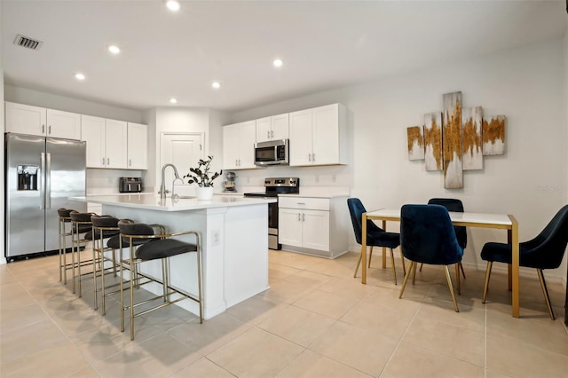 kitchen with a kitchen breakfast bar, light tile patterned floors, an island with sink, white cabinetry, and stainless steel appliances