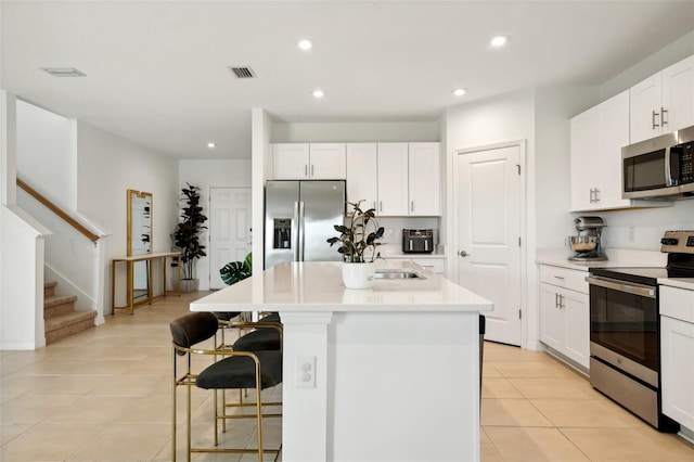 kitchen featuring white cabinetry, a kitchen island with sink, light tile patterned flooring, and appliances with stainless steel finishes