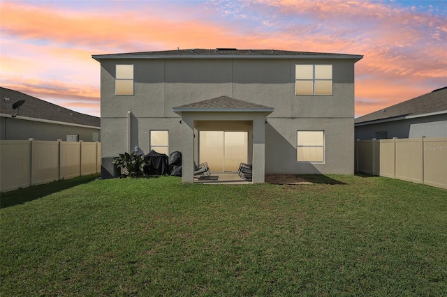 back house at dusk with a lawn and a patio