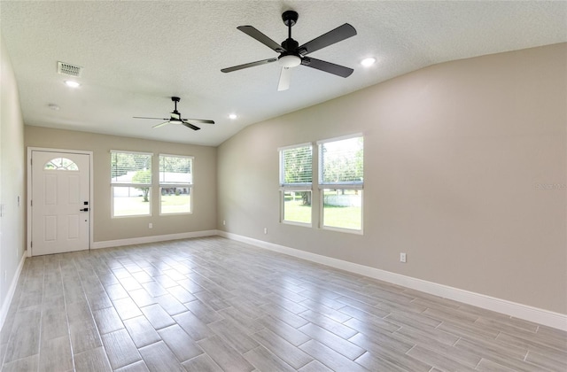 empty room with a healthy amount of sunlight, light wood-type flooring, vaulted ceiling, and a textured ceiling