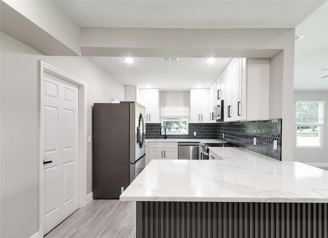 kitchen with white cabinetry, kitchen peninsula, a healthy amount of sunlight, and stainless steel appliances