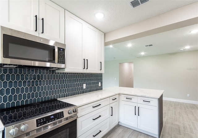 kitchen featuring white cabinets, kitchen peninsula, backsplash, light stone countertops, and appliances with stainless steel finishes