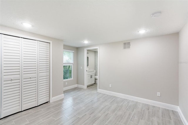 unfurnished bedroom with ensuite bathroom and light wood-type flooring