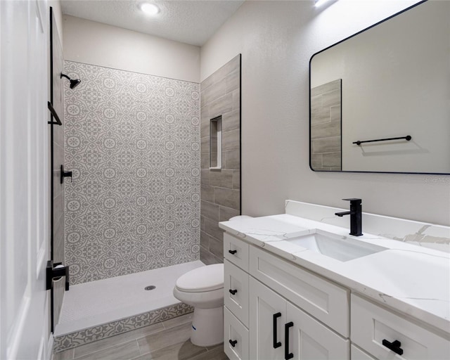 bathroom featuring vanity, toilet, a textured ceiling, and tiled shower