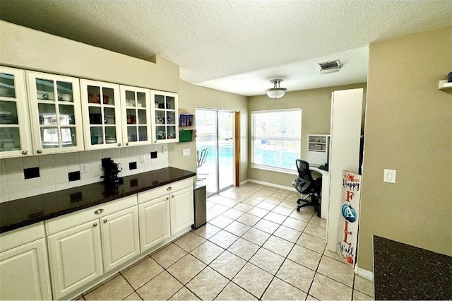 kitchen featuring decorative backsplash, light tile patterned floors, a textured ceiling, and white cabinetry