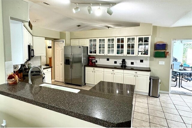 kitchen featuring kitchen peninsula, stainless steel fridge, decorative backsplash, light tile patterned floors, and white cabinets