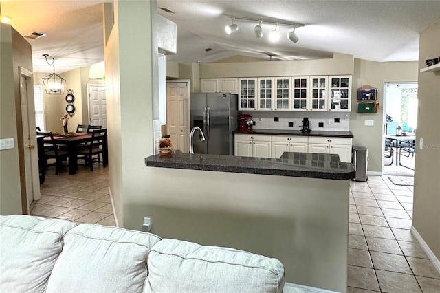 kitchen featuring kitchen peninsula, stainless steel refrigerator with ice dispenser, vaulted ceiling, white cabinets, and light tile patterned flooring