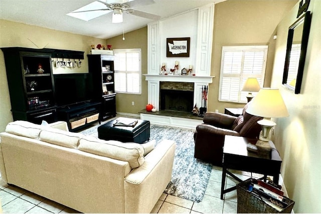 tiled living room with a wealth of natural light, a fireplace, ceiling fan, and vaulted ceiling with skylight