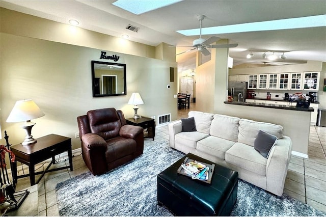 living room featuring ceiling fan, vaulted ceiling with skylight, and light tile patterned flooring