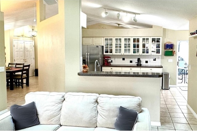 kitchen with white cabinetry, kitchen peninsula, stainless steel fridge, and vaulted ceiling