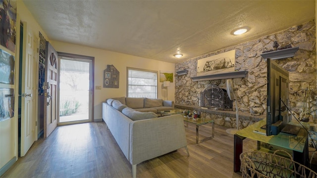 living room featuring a textured ceiling, hardwood / wood-style floors, and a stone fireplace