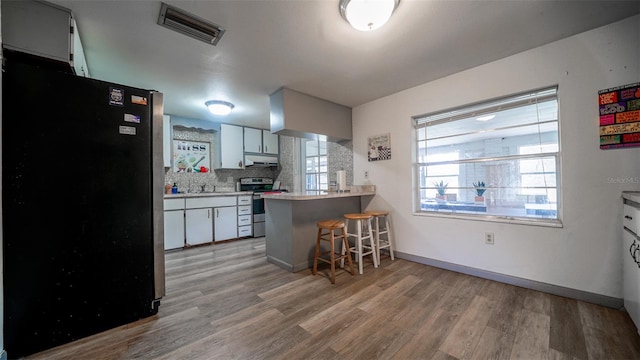 kitchen with a kitchen bar, kitchen peninsula, appliances with stainless steel finishes, decorative backsplash, and white cabinets