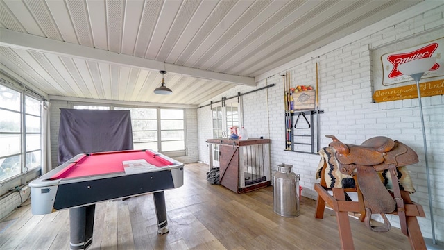 rec room featuring a barn door, hardwood / wood-style floors, beamed ceiling, brick wall, and pool table