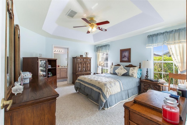 bedroom with ensuite bath, ceiling fan, a raised ceiling, and light colored carpet