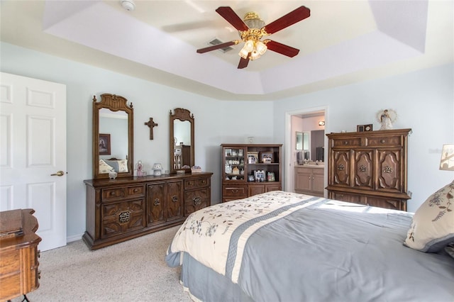 carpeted bedroom featuring connected bathroom, a raised ceiling, and ceiling fan