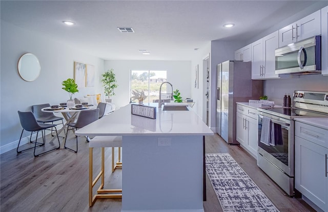 kitchen featuring stainless steel appliances, an island with sink, a breakfast bar, white cabinets, and light hardwood / wood-style flooring